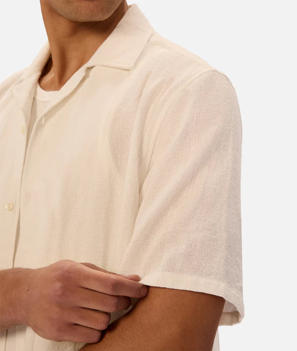 Close-up of a person wearing a beige short-sleeve shirt on a white background