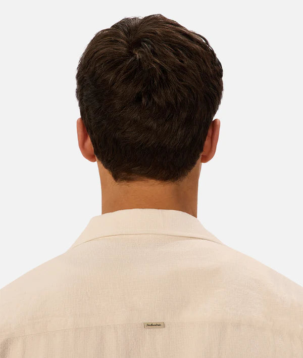 Back view of a person wearing a beige shirt with a visible brand logo on a white background