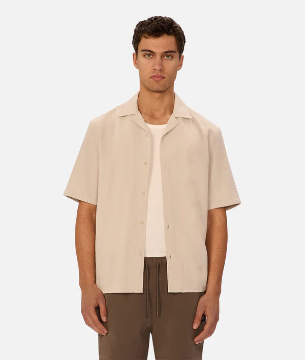 Man wearing a beige short-sleeve shirt over a white shirt on a plain background