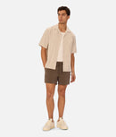 Man wearing a beige shirt and brown shorts on a white background