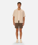 Man wearing a beige shirt and brown shorts on a white background
