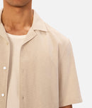 Beige short-sleeve shirt worn by a person on a white background