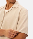 Beige short-sleeve shirt worn by a person on a white background