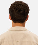 Back view of a person wearing a beige shirt with a visible brand logo on a light background