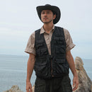 A person wearing a black multi-pocket vest, standing outdoors.