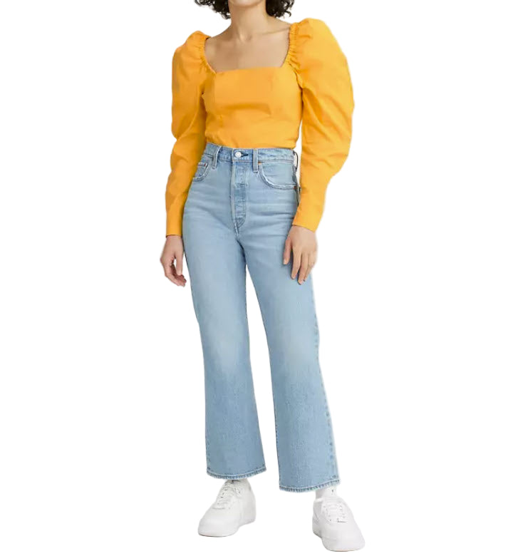 Person wearing a yellow top with puffed sleeves and light blue jeans on a white background
