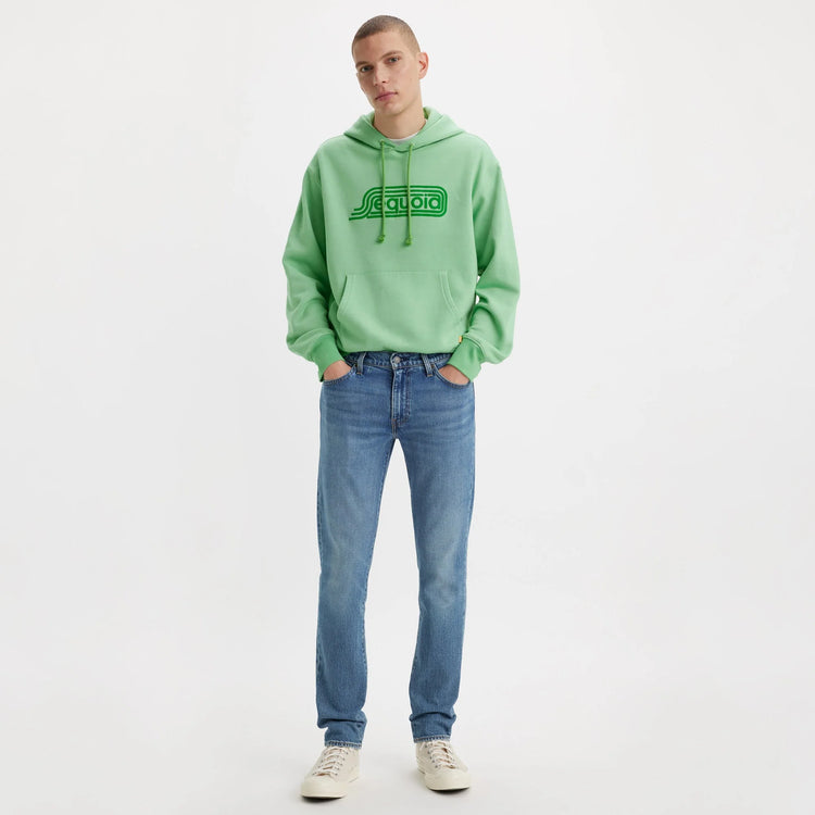 Person wearing a green hoodie with a logo and blue jeans on a white background