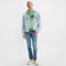 Person wearing a light blue denim jacket, green hoodie, and jeans on a white background