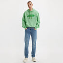 Person wearing a green hoodie with a logo and blue jeans on a white background