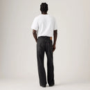 A model shown from the back wearing a white t-shirt and dark gray wide-leg jeans, photographed against a neutral light gray studio background.