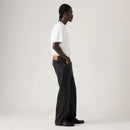 Person wearing a white t-shirt and black jeans standing against a plain background