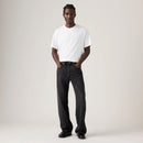 Man wearing a white t-shirt and black jeans on a plain background