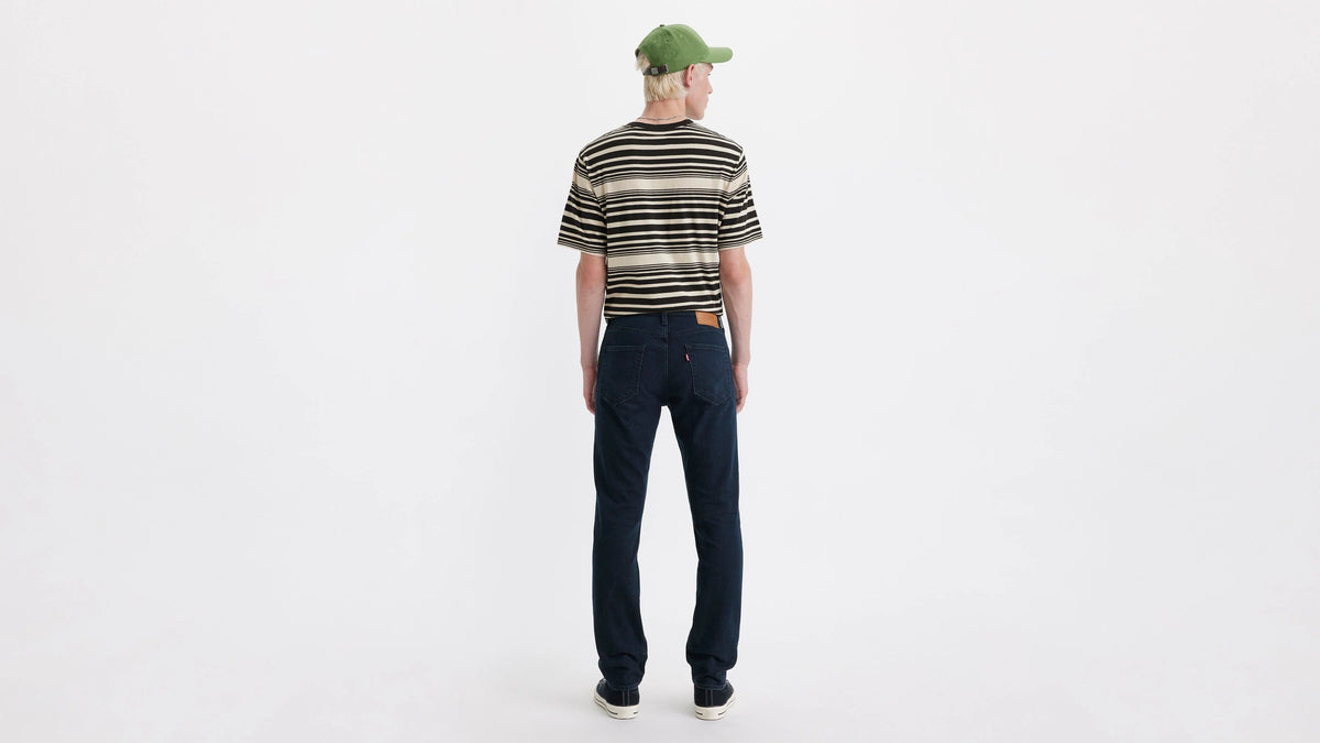 Person wearing a striped shirt, dark jeans, and a green cap on a white background
