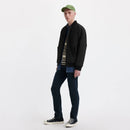 Person wearing a black jacket, striped shirt, jeans, and green cap on a white background