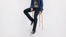 Person wearing dark jeans and a blue jacket sitting on a stool against a white background