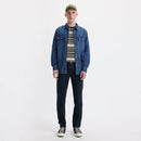 Man wearing a blue denim jacket, striped shirt, and dark jeans on a white background