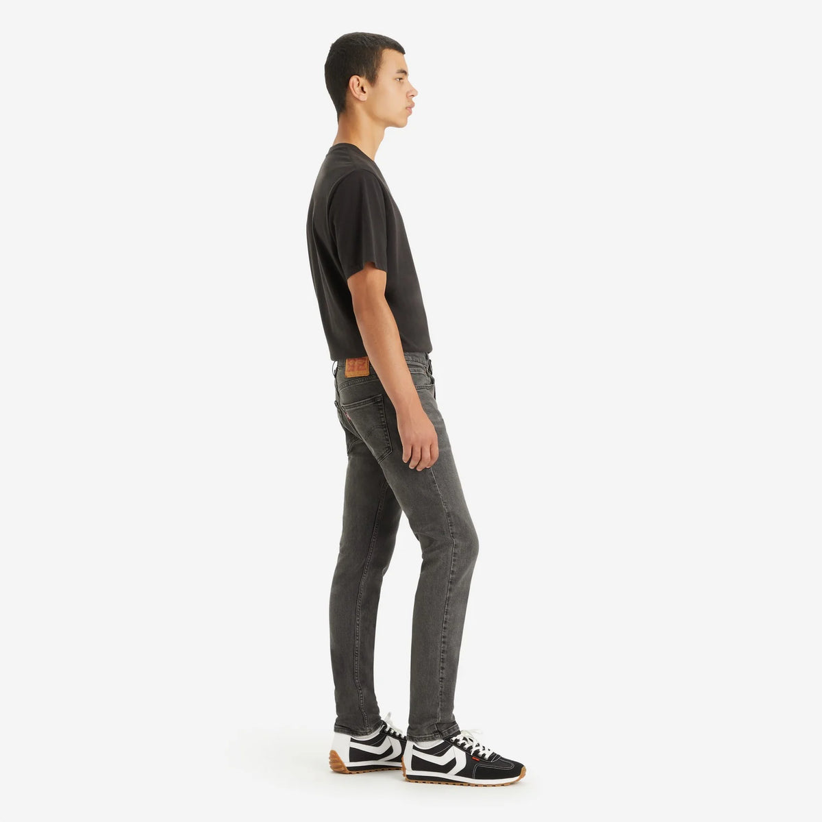 Person wearing black t-shirt and gray jeans standing against a white background