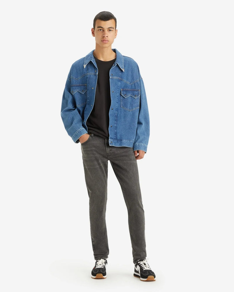 Man wearing a blue denim jacket and gray jeans on a white background