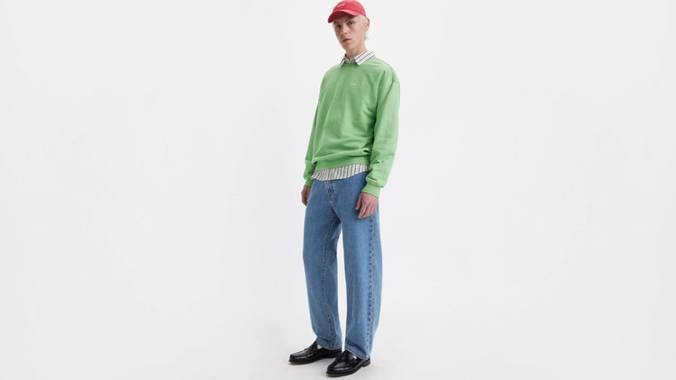 Person wearing a green sweater and blue Levi's jeans on a white background
