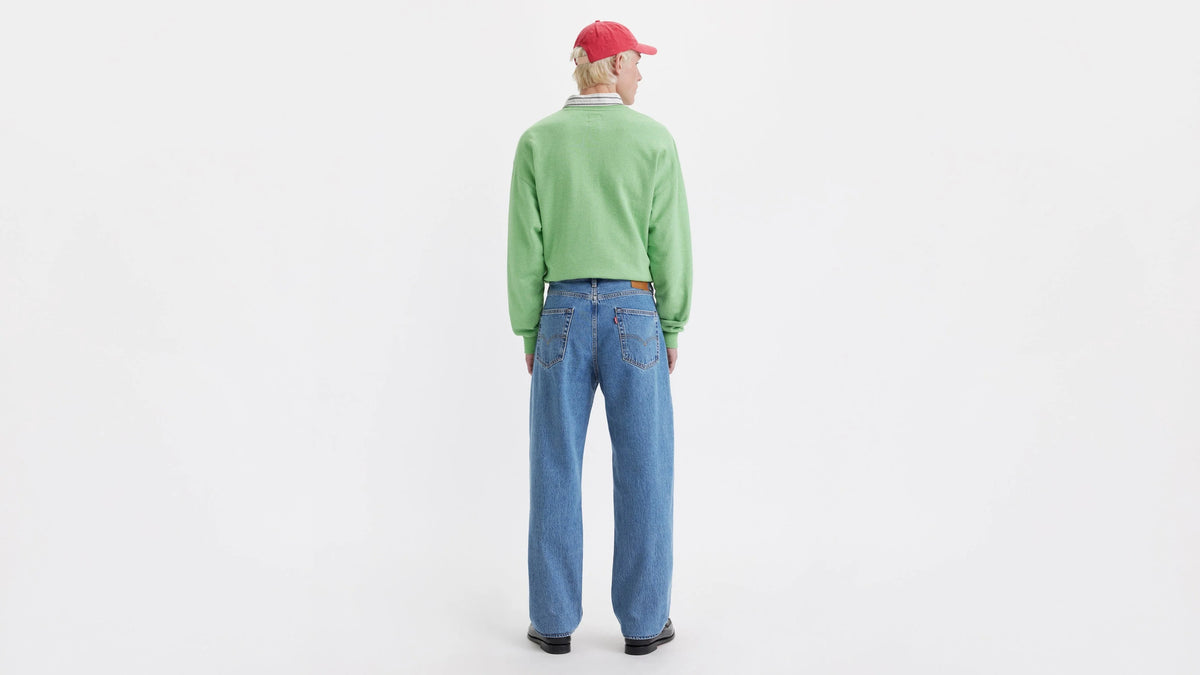 Person wearing a green sweater and blue jeans on a white background