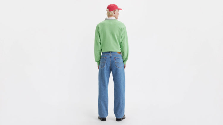 Person wearing a green sweater and blue jeans on a white background