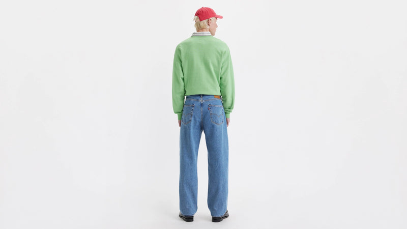 Person wearing a green sweater and blue jeans on a white background