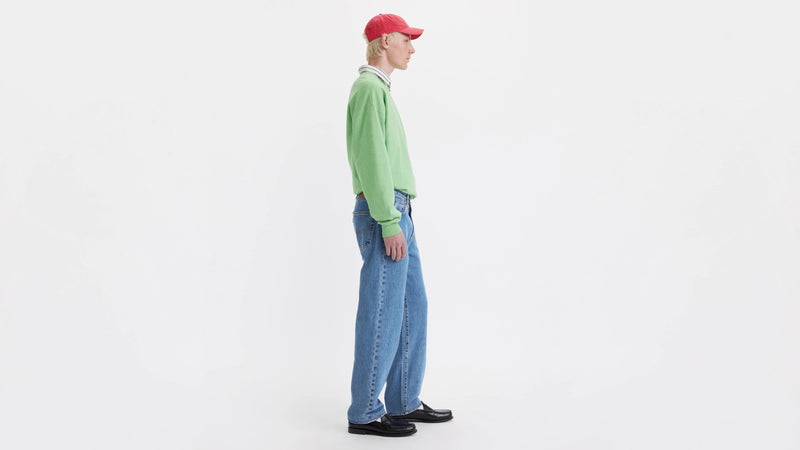Person wearing a green sweater, blue jeans, and a red cap on a white background