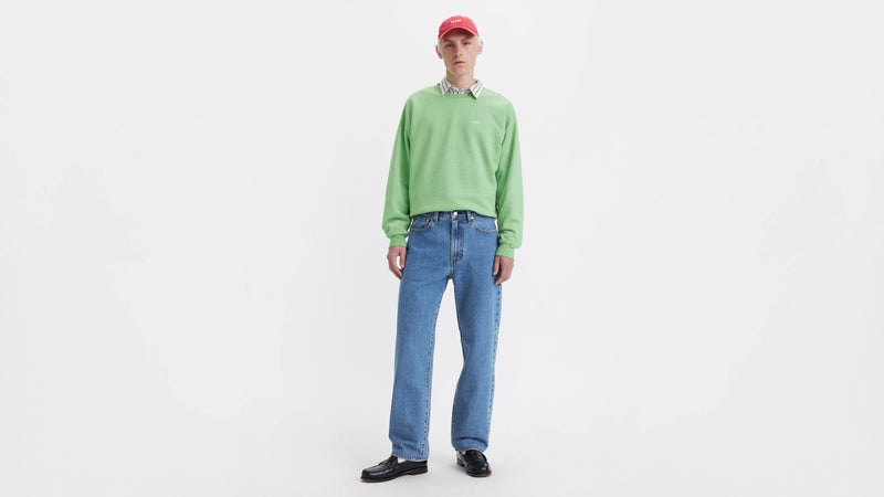 Person wearing a green sweater and blue jeans on a white background