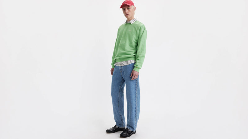 Person wearing a green sweater and blue Levi's jeans on a white background