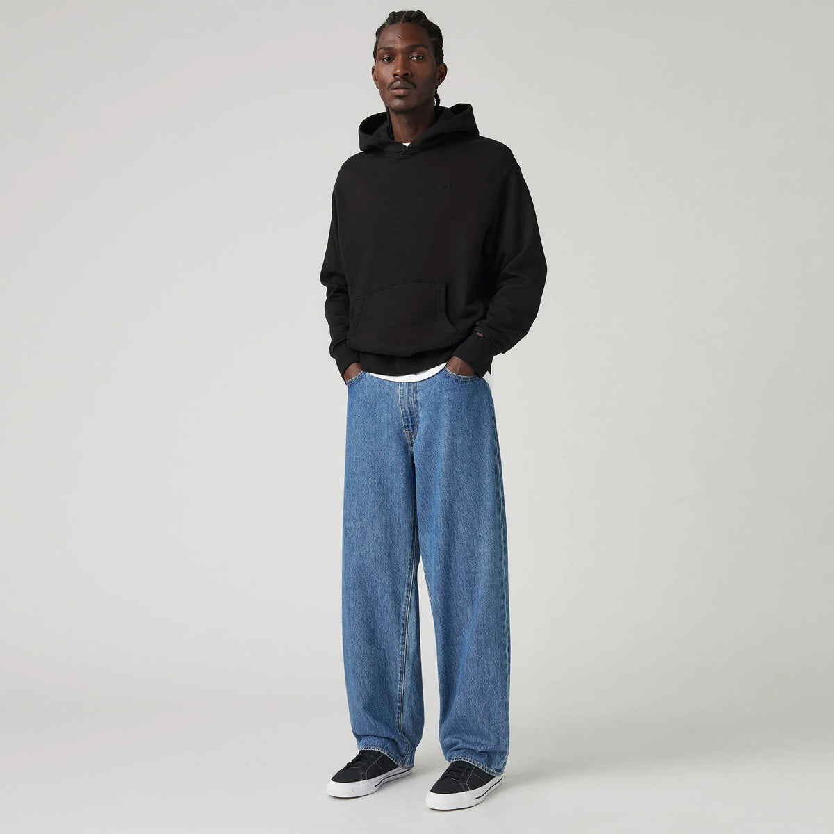 Person wearing a black hoodie and blue jeans on a white background