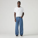 Man wearing a white t-shirt and blue jeans on a plain background