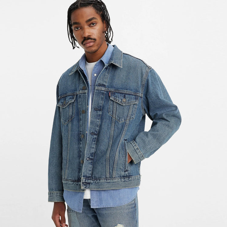 A man wearing a relaxed fit trucker jacket in a blue denim color, with Levi's branding visible on the collar and cuffs.