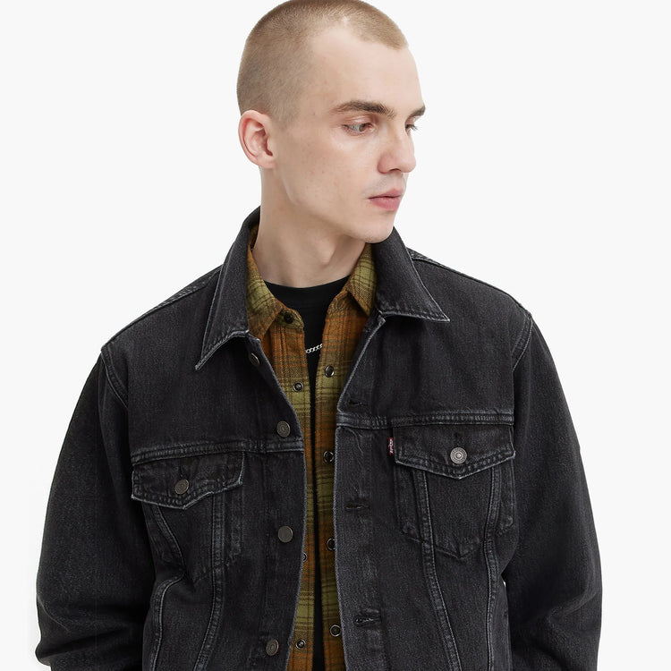 Man wearing a black denim jacket over a plaid shirt on a white background