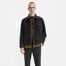 Man wearing a black denim jacket over a plaid shirt on a white background