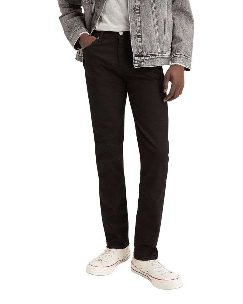 Man wearing a gray denim jacket, white shirt, black pants, and white sneakers on a white background