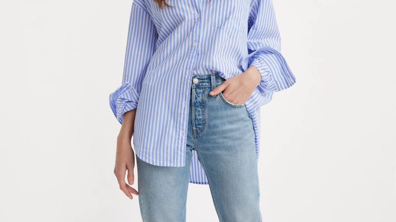 Person wearing a blue and white striped shirt and light blue jeans on a plain background