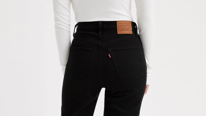 Person wearing black pants with a brown leather patch on a white background