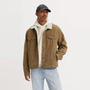 A male model wearing a beige Levi's Type III Sherpa Trucker Jacket with a white shirt and blue jeans, with a cap on his head.
