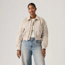 Person wearing a beige jacket and light blue jeans on a plain background