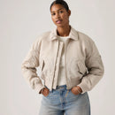 Woman wearing a beige bomber jacket and blue jeans on a plain background