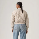 Person wearing a beige bomber jacket and light blue jeans on a plain background