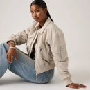 Woman wearing a beige jacket and blue jeans sitting on a white background