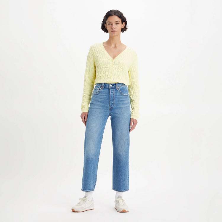 Woman wearing a yellow sweater and blue jeans on a white background