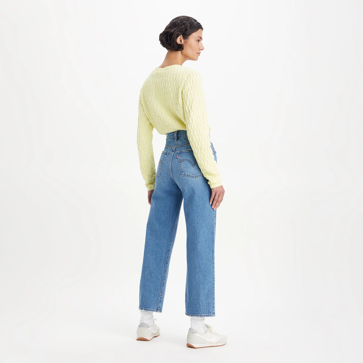 Person wearing a light yellow sweater and blue jeans on a white background