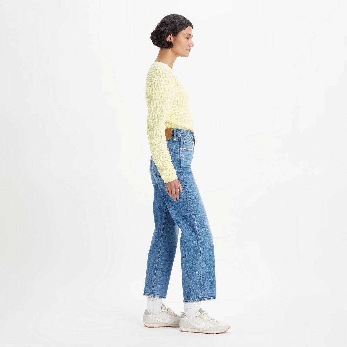 Person wearing a light yellow sweater and blue jeans on a white background