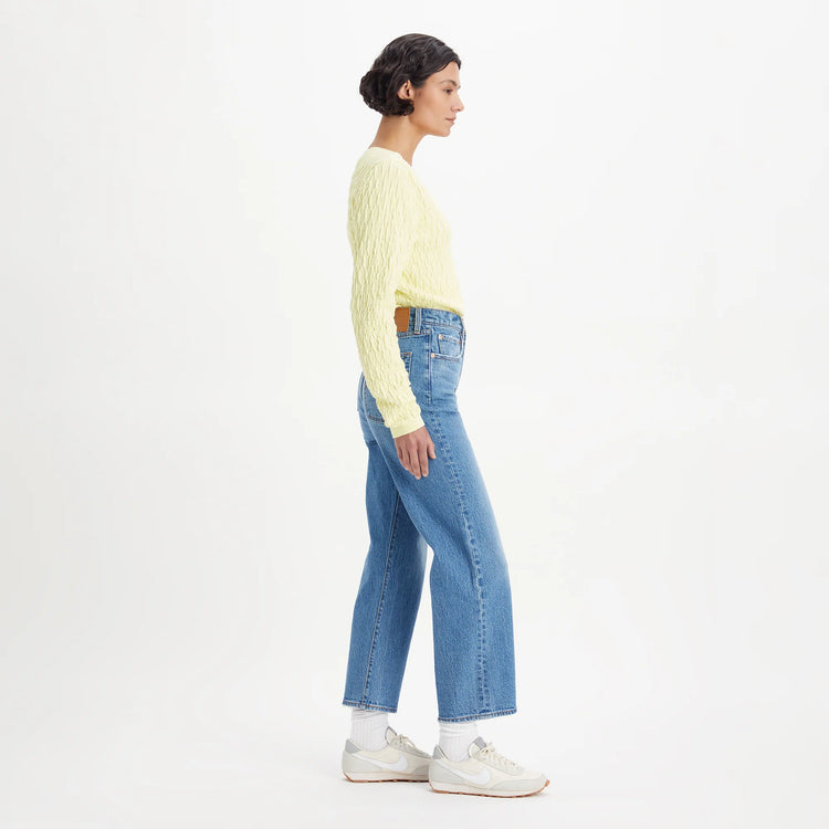 Person wearing a light yellow sweater and blue jeans on a white background