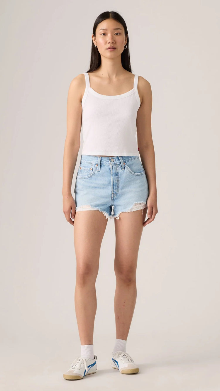Woman wearing Levi's light blue denim shorts and a white tank top on a plain background