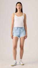 Woman wearing Levi's light blue denim shorts and a white tank top on a plain background