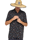Person wearing a dark patterned shirt and straw hat on a plain background