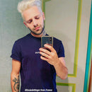 Man with platinum blonde hair taking a mirror selfie wearing a navy blue t-shirt.
